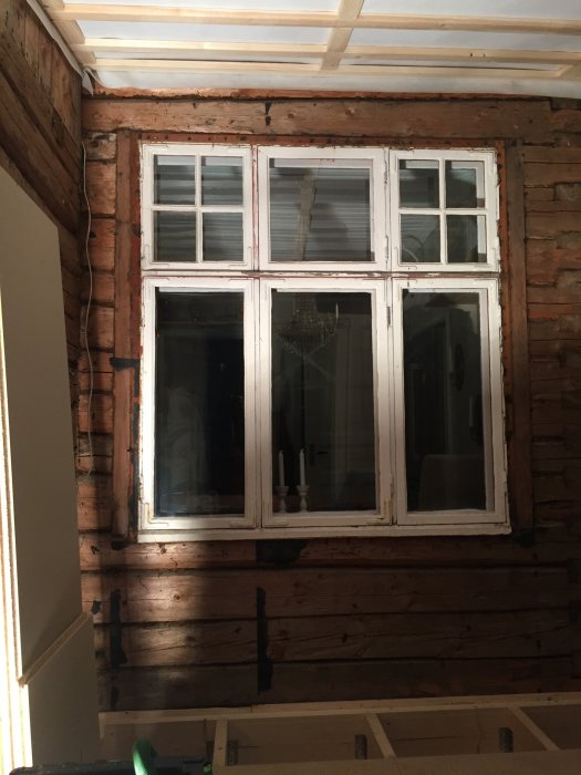 Fönster i träfasad på tillbyggt hus med synliga stockar och syllar, i förberedelse för renovering.
