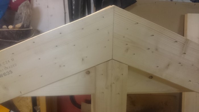 Närbild på en nyligen konstruerad takstol i trä, förstärkt med många spikar och limmad plywood.