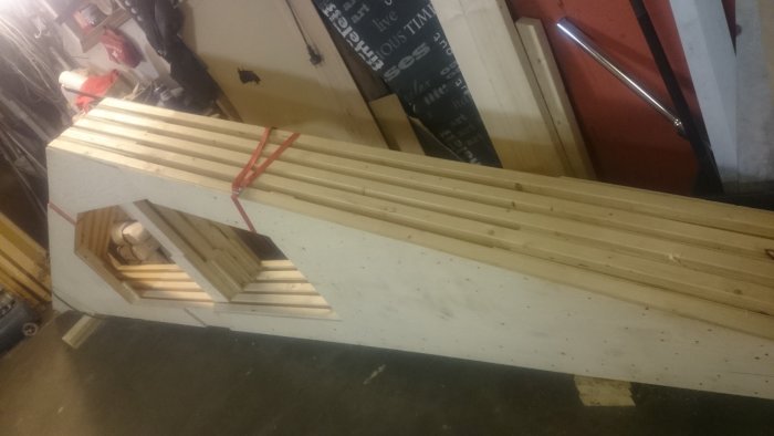 Fem nybyggda trä-takstolar staplade i ett garage, förstärkta med plywood och säkrade med remmar för byggprojekt.