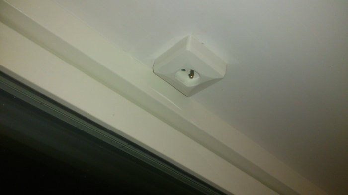 Utanpåliggande vitt lamputtag placerat på en vägg nära taket, ovanför ett fönster.