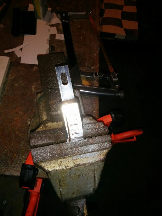 Metallstycke i skruvstäd med verktyg och pappersmallar på arbetsbänken, förberedelse för zinklödning.