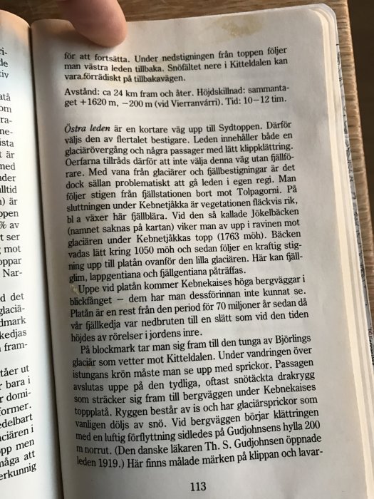 En sida från boken "På fjälltur", med text som beskriver leder och terräng för fjällvandring, hållen öppen av en hand.