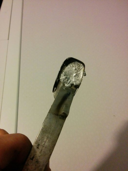 En närbild av en metallbit med smält och omformad zink fastsatt vid änden, resultatet av en hemmagjord smältprocess.