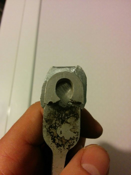 Metallbit med ovalt hål och slipmärken hålls av en hand, visar DIY metallbearbetning.