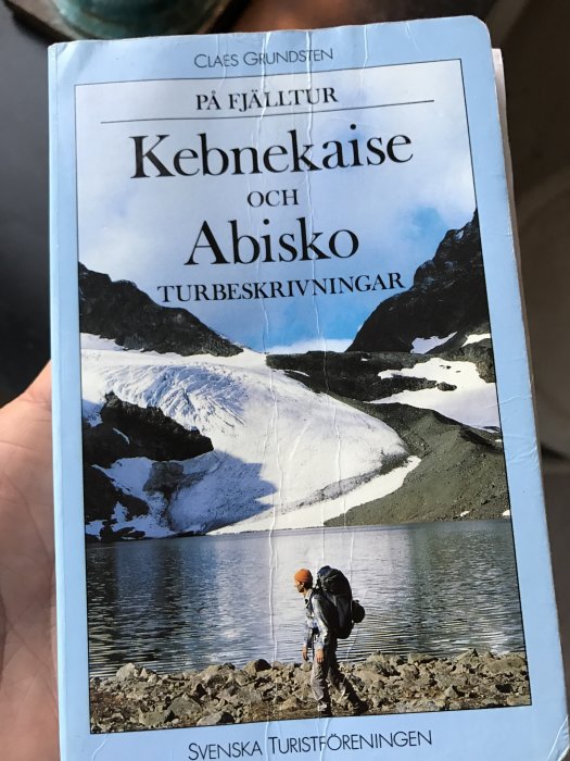 Bokomslag "På fjälltur Kebnekaise och Abisko" med vandrare framför fjällsjö och snöklädda toppar.