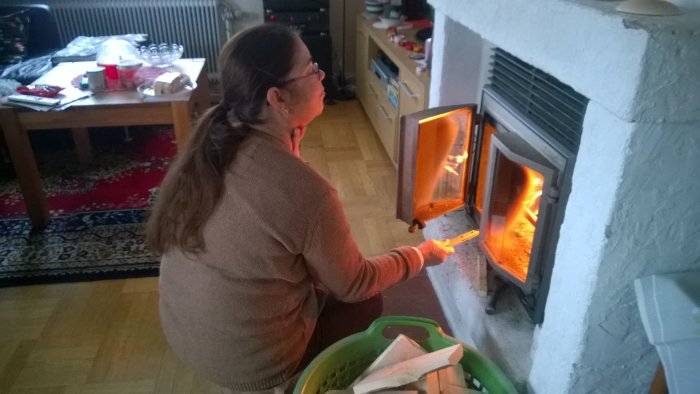 Kvinna tänder en vedeldad braskamin av märket Keddy, inomhusmiljö med synlig eld och ved.