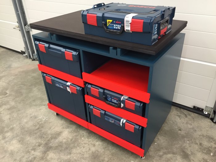 Anpassat arbetsbord med förvaring och L-Boxx-system i björkplywood, röda hyllor och svarta bordsskivor.