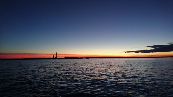 Solnedgång över hav med silhuett av en anläggning vid horisonten och färgglad himmel.