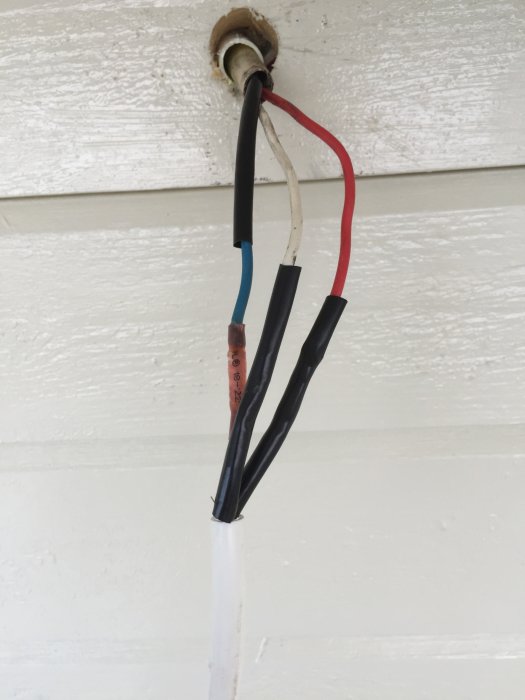 Elektriska ledningar med krympslang över en skarv, redo för en ny lampa på en vit vägg.