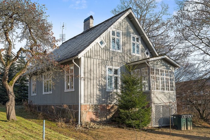 Exteriör av en tvåvånings villa från 1915 med träfasad och vitmålade fönster, belägen i en trädgård.