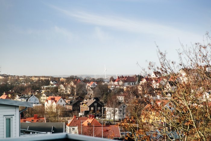 Utsikt över villaområde med pittoreska hus och fjärran vindkraftverk i dagsljus.