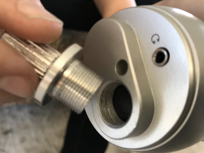 Någons hand håller en metallmikrofon med en skruv nära mikrofonens gängade hål, där gängorna inte matchar.