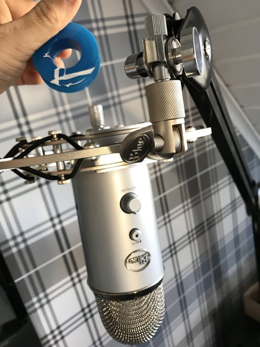 Hand håller gängtejp nära ett mikrofonstativ och mikrofon mot rutig bakgrund.