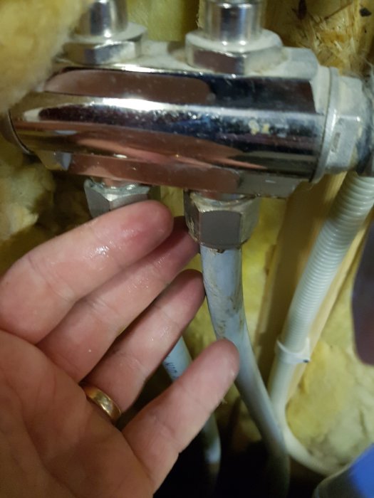 En hand som känner på en droppande vattenkoppling under en kran.