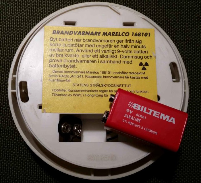 Öppen brandvarnare med infoetikett och nytt 9V-batteri redo för utbyte.