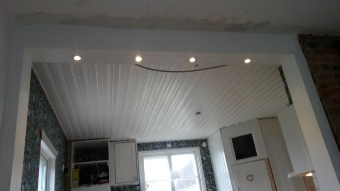 Inredning under renovering med synlig murstock, tak med inbyggda spotlights och en delvis tapetserad vägg.