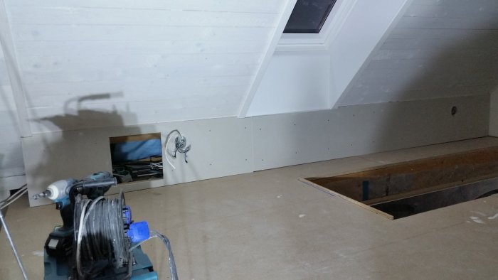 Ombyggnation av ett loft med låga väggar, där elinstallationer och en inspektionslucka syns. En borr och kabelvinda i förgrunden.