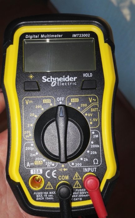 Digital multimeter från Schneider Electric hållen i hand, modell IMT23002 med svart gult hölje.