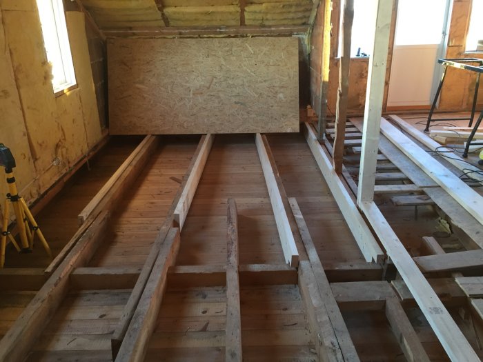 Interiör av hus under renovering med synliga golvbjälkar och isolering.