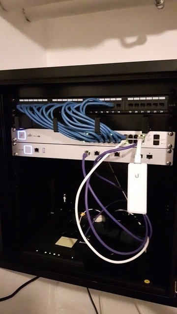 Unifi POE Switch och Security Gateway monterade i nätverksskåp med ordnade blå och lila kablar.