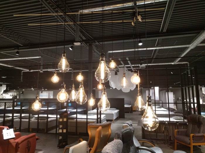 Möbelbutik interiör med exponerade taklampor, soffor och sängar, industrikänsla med synlig takstruktur.