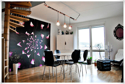 Modernt vardagsrum med stort blommönstrat konstverk, trägolv och spiraltrappa.