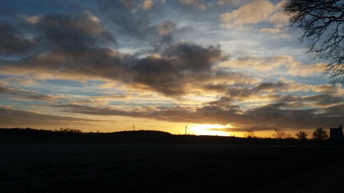 Soluppgång över ett frosttäckt landskap med sällsynta moln och en vindkraftverkssilhuett.