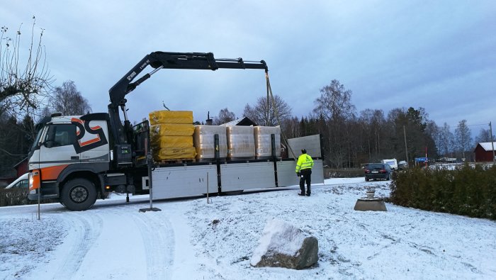 Lastbil levererar Isover takisolering med vindpapp på en snöig tomt.