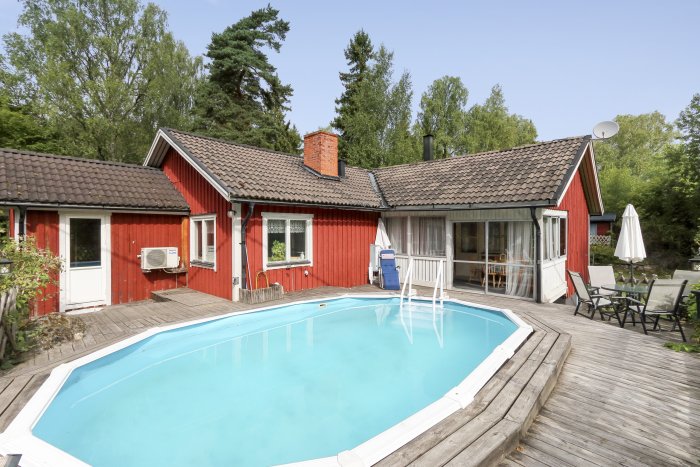 Ett rött enplanshus med trädäck och nedsänkt pool på landsbygden, i behov av renovering och uppfräschning.