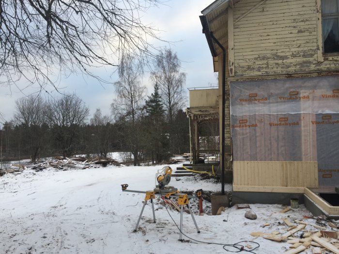 Husunderhåll under vintern med synlig isolering, verktyg i snön och en sjö i bakgrunden.