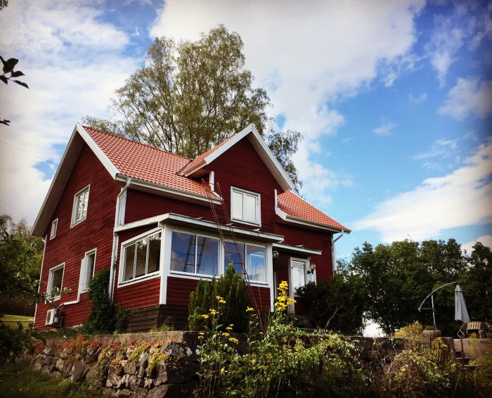 Rödmålat hus med nylagt tak och vitmålat uterum under en solig himmel.