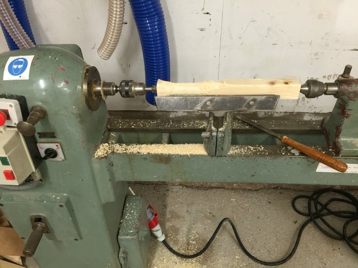 En träregel spänd på en svarv med spån och en svarvjärn i en verkstad.