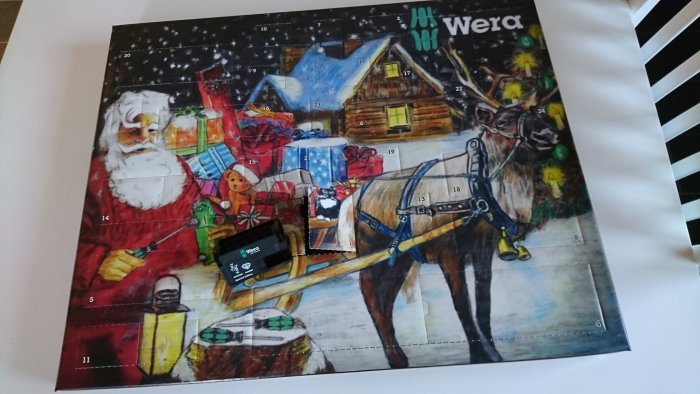 Öppnad julkalender med verktygstema, med julklappar, tomten och en ren.