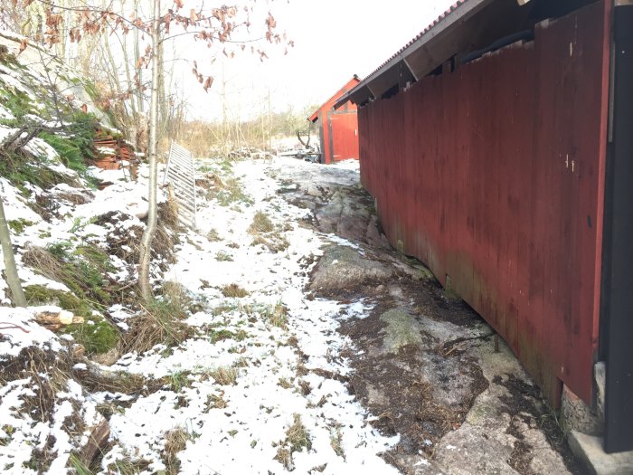 Rött uthus byggt på sluttande berghällar med snörester, lutande in mot husets sida.