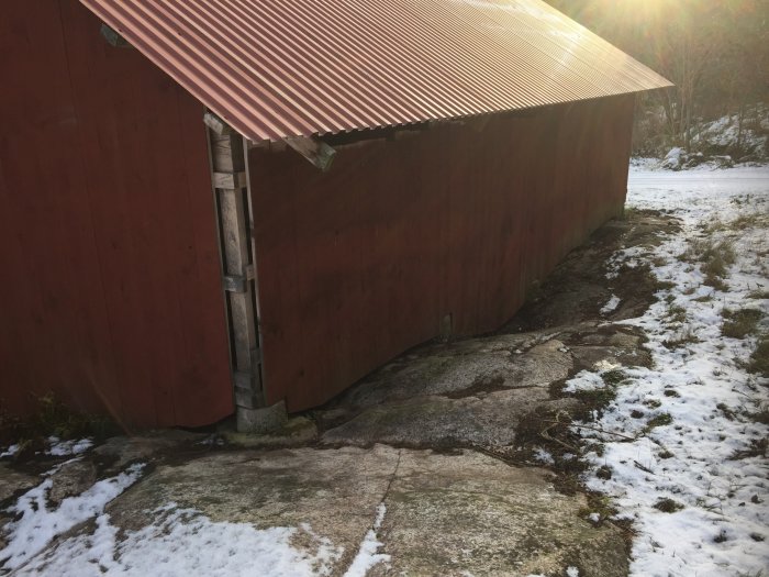 Rött uthus byggt direkt på sluttande berghällar med snötäckt mark runtomkring.