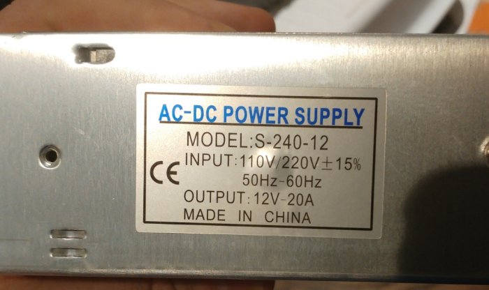 AC-DC-transformator med specifikationsetikett som visar modellnummer, input-, output-värden och tillverkningsland.