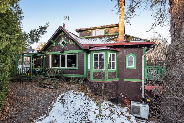 Välbevarat äldre hus i speciell stil med gröna snickerier, veranda och snöfläckar på marken.