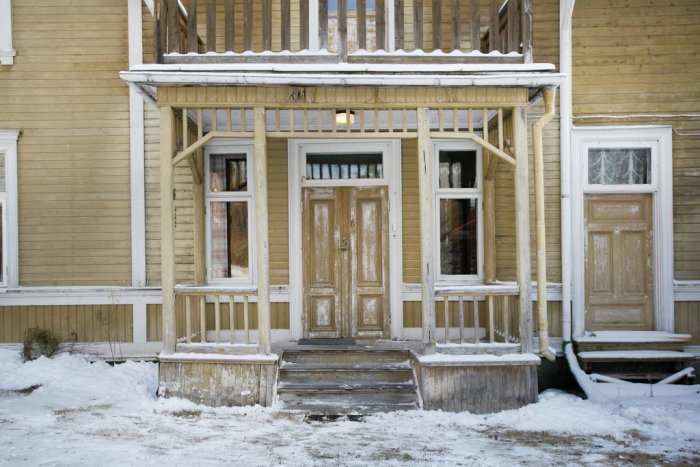 Välbevarad entré till äldre trähus med snö och detaljerad snickeri.