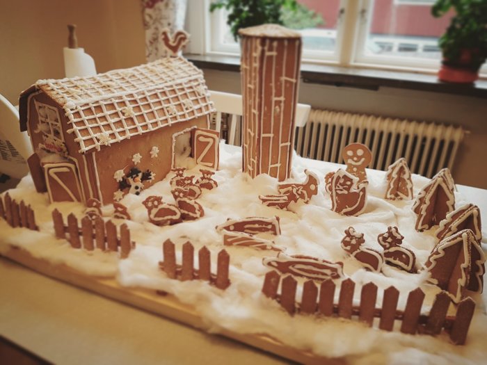 Pepparkaksbondgård med hus, silo och figurer omgivna av staket på snötäckt underlag.