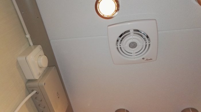 Takmonterad frånluftsfläkt och strömbrytare i ett badrum.