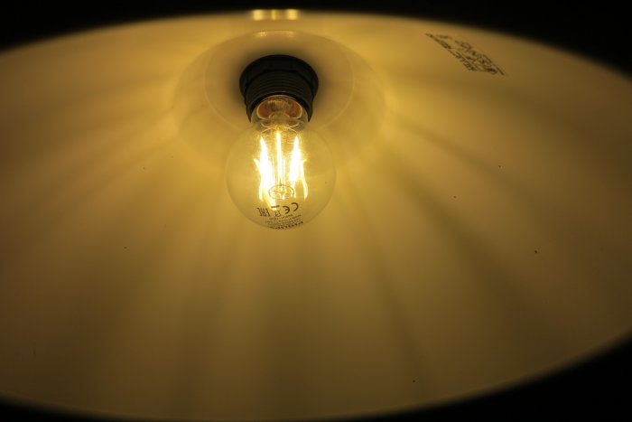 Tänd glödlampa med varmvit ljussken 2700K mot en ljus yta, utan synbart gult glas.