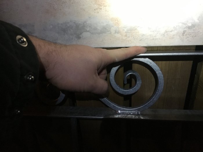 Hand pekar på en dekorativ spiral i ett metallstaket mot en suddig bakgrund.