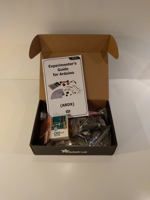 Öppnad Adafruit förpackning med Arduino Experiment Kit och guidebok synlig.