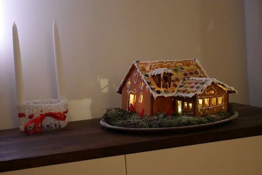 Pepparkakshus modell av Fiskarhedenvillan Näktergalen med julbelysning och dekor på fat med ljus.