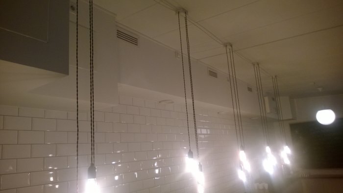 Vitt kakel i badrum med industriella lampor hängandes på sladdar.