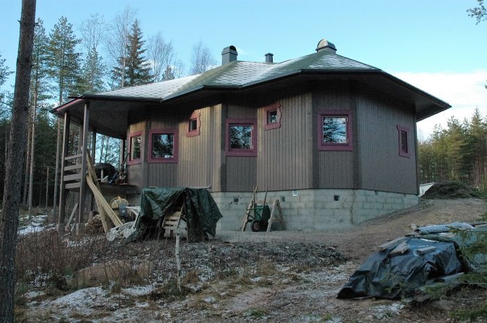 Nybyggt fritidshus på 90 kvm i skogsmiljö med träfasad och röda fönsteromfattningar, snickarbod och skog i bakgrunden.