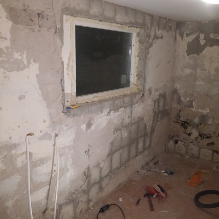 Renoveringsprojektets väggar med avskalad puts, exponerade betongblock, ett fönster och verktyg på golvet.
