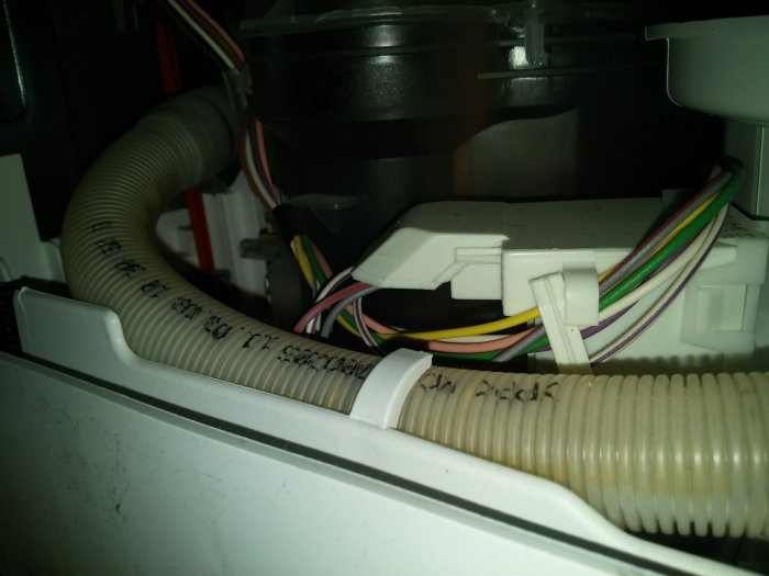 Trångt utrymme inuti en apparat med en smutsig slang och färgmärkta elkablar som behöver rengöras.