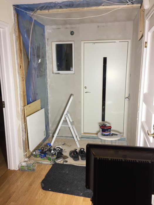 Renoveringsarbete på en hall med oskyddade väggar, elskåp och arbetsmaterial på golvet.