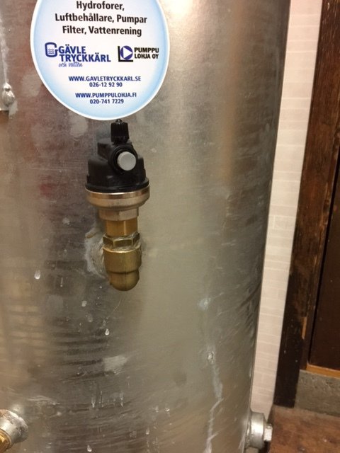 Hydrofortank med fäst rör och tryckmätare, inklusive etiketter för företag och underhåll av pumpsystem.
